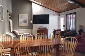 A dining area with a wooden table and chairs, a television mounted on the wall, and a sofa in the background. - Spacious 11BR Cabin for Groups | Near Granby Ranch (Granby)