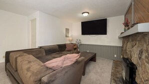 Un salon comprenant un canapé d’angle, un téléviseur à écran plat fixé au mur, une cheminée et un mur décoratif en pierre.