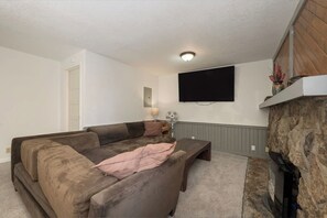 A living room with a sectional sofa, a flat-screen TV mounted on the wall, a fireplace, and a stone accent wall. - Spacious 11BR Cabin for Groups | Near Granby Ranch (Granby)