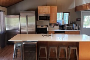 A modern kitchen with stainless steel appliances, a large island, and bar stools. - Spacious 11BR Cabin Near Granby Ranch + Free Belize Week (Granby)