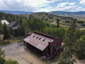 A wooden cabin with a metal roof, surrounded by trees and a hilly landscape. - Spacious 11BR Cabin for Groups | Near Granby Ranch (Granby)