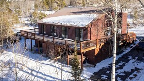 Une cabane dotée d’une terrasse, entourée de neige et d’arbres.