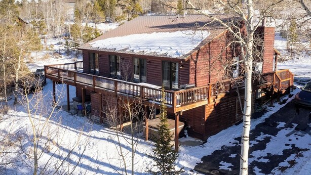 A cabin with a deck, surrounded by snow and trees.