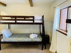 A bunk bed with a patterned bedspread and pillows, a window with curtains, and a carpeted floor. - Spacious 11BR Cabin for Groups | Near Granby Ranch (Granby)