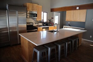 A modern kitchen with stainless steel appliances, wooden cabinets, and a central island with stools. - Spacious 11BR Cabin for Groups | Near Granby Ranch (Granby)