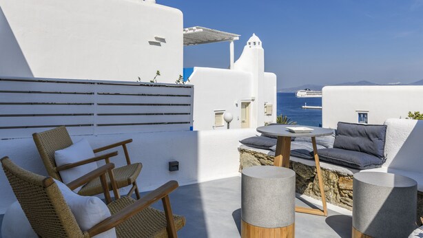 A white-walled terrace with wicker chairs and a round table, overlooking the sea. - Mykonos Perla Town House - Perfect Location with Pool and Private Parking - 2 BR (Mykonos)