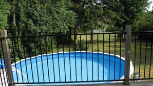Une piscine dotée d’une terrasse en bois et d’une rambarde en métal, entourée d’arbres.