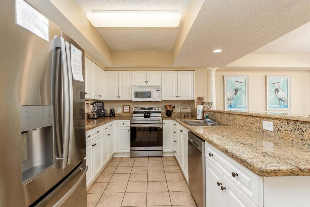 A kitchen with white cabinets, stainless steel appliances, a granite countertop, and a tiled floor.