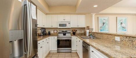 A kitchen with white cabinets, stainless steel appliances, a granite countertop, and a tiled floor.