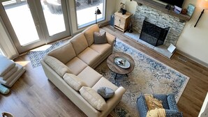 En rummelig stue med en beige modulsofa, en blå sofa med mønster, et sofabord og en pejs med en væg i natursten.