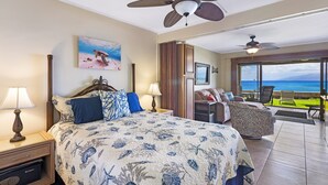 Een slaapkamer met een bed, nachtkastjes, een plafondventilator en uitzicht op de oceaan door grote ramen.