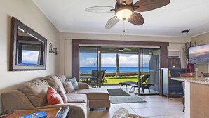 Een woonkamer met een groot raam, een plafondventilator en een eethoek met uitzicht op de oceaan.