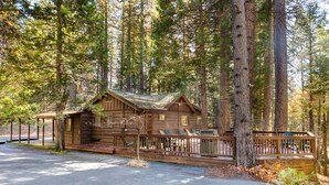 A rustic cabin with a wooden deck and a stone foundation, surrounded by tall pine trees. - (50R) Soots - Me at The Redwoods In Yosemite (Yosemite National Park)