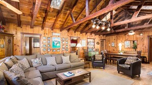 A cozy log cabin interior with a large sectional sofa, a coffee table, and a dining area with a wooden table and chairs. - (50R) Soots - Me at The Redwoods In Yosemite (Yosemite National Park)