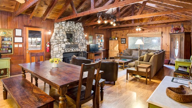 A rustic cabin interior with a stone fireplace, wooden dining table, and a cozy living area with sofas and a television. - (50R) Soots - Me at The Redwoods In Yosemite (Yosemite National Park)