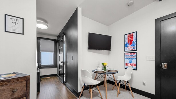 Habitación de hotel moderna con comedor, televisor de pantalla plana y puerta con cámara de seguridad.