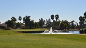 Ein Golfplatz mit einem Wasserspeier, gepflegtem Rasen, Palmen und einem Teich.