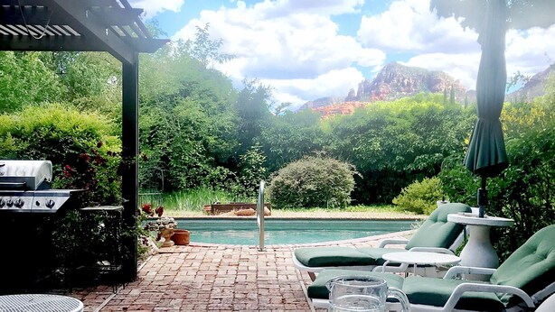 An outdoor patio with a pool, lounge chairs, and a table with drinks and snacks.
