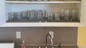 Een keuken met een dubbele spoelbak, een afwasmiddelfles en bovenkasten met diverse glazen.