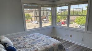 Een slaapkamer met een groot erkerraam, een bed met een geborduurd beddegoed en uitzicht op de straat.