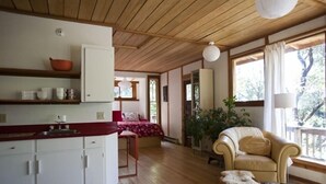 A cozy room with a wooden ceiling, a bed with a red and white patterned bedspread, a beige armchair, a small ottoman, and a plant. - A Happy Nest up in the trees, unique Salt Spring Cottage close to town (Salt Spring Island)