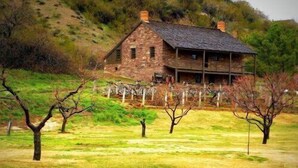 Una casa de piedra con porche, rodeada por un campo cubierto de hierba y árboles.