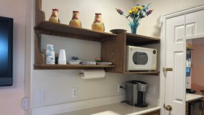 Una cocina con microondas, cafetera y estantes de madera decorados.