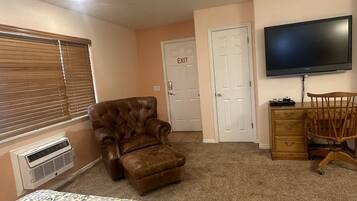 A bedroom with a large bed, a brown leather armchair, a wooden dresser, a television, and an exit door.