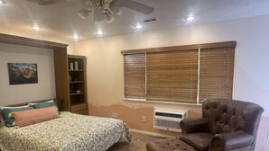 Un dormitorio con cama, cómoda, ventana con persianas, ventilador de techo y aire acondicionado.