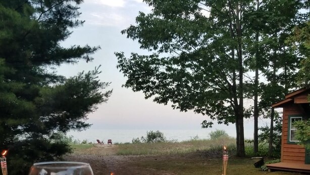 A wooden deck with a glass of red wine, a fire pit, and a small cabin in the background.