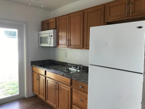 A kitchen with wooden cabinets, a white refrigerator, a stainless steel sink, and a microwave. - Pompano Breeze (Pompano Beach)