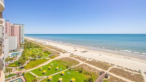 A beachfront hotel with multiple floors, a pool, and a beach area with umbrellas. - Newly renovated, modern, ocean front, prime location!  Walk to everything! (Myrtle Beach)