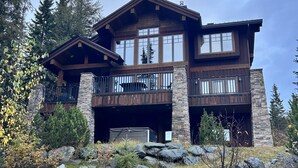 A two-story log cabin with a stone foundation, large windows, and a balcony.