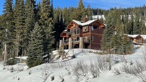 A lodge with a wooden exterior and multiple balconies, surrounded by snow-covered ground and tall evergreen trees.