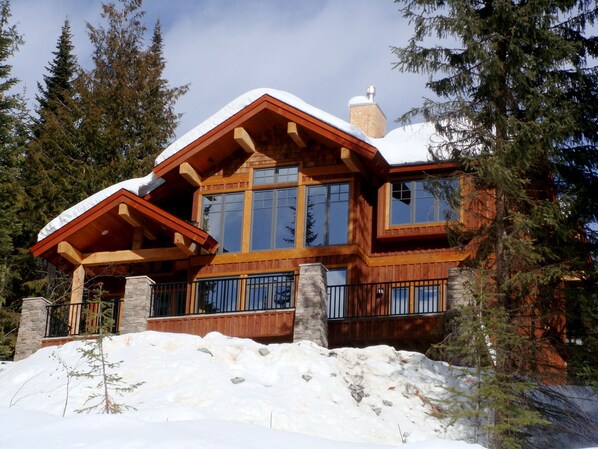A large, multi-story wooden house with a snow-covered roof, surrounded by tall evergreen trees. - Family Friendly Mountain View Luxury Chalet (Sun Peaks)