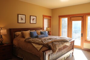 A bedroom with a large bed, two framed deer pictures on the wall, a nightstand with a lamp, and a view through the door. - Family Friendly Mountain View Luxury Chalet (Sun Peaks)