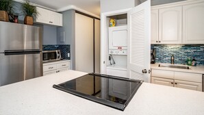 Una cocina moderna con estufa integrada, electrodomésticos de acero inoxidable, armarios blancos y un salpicadero de azulejos azules.