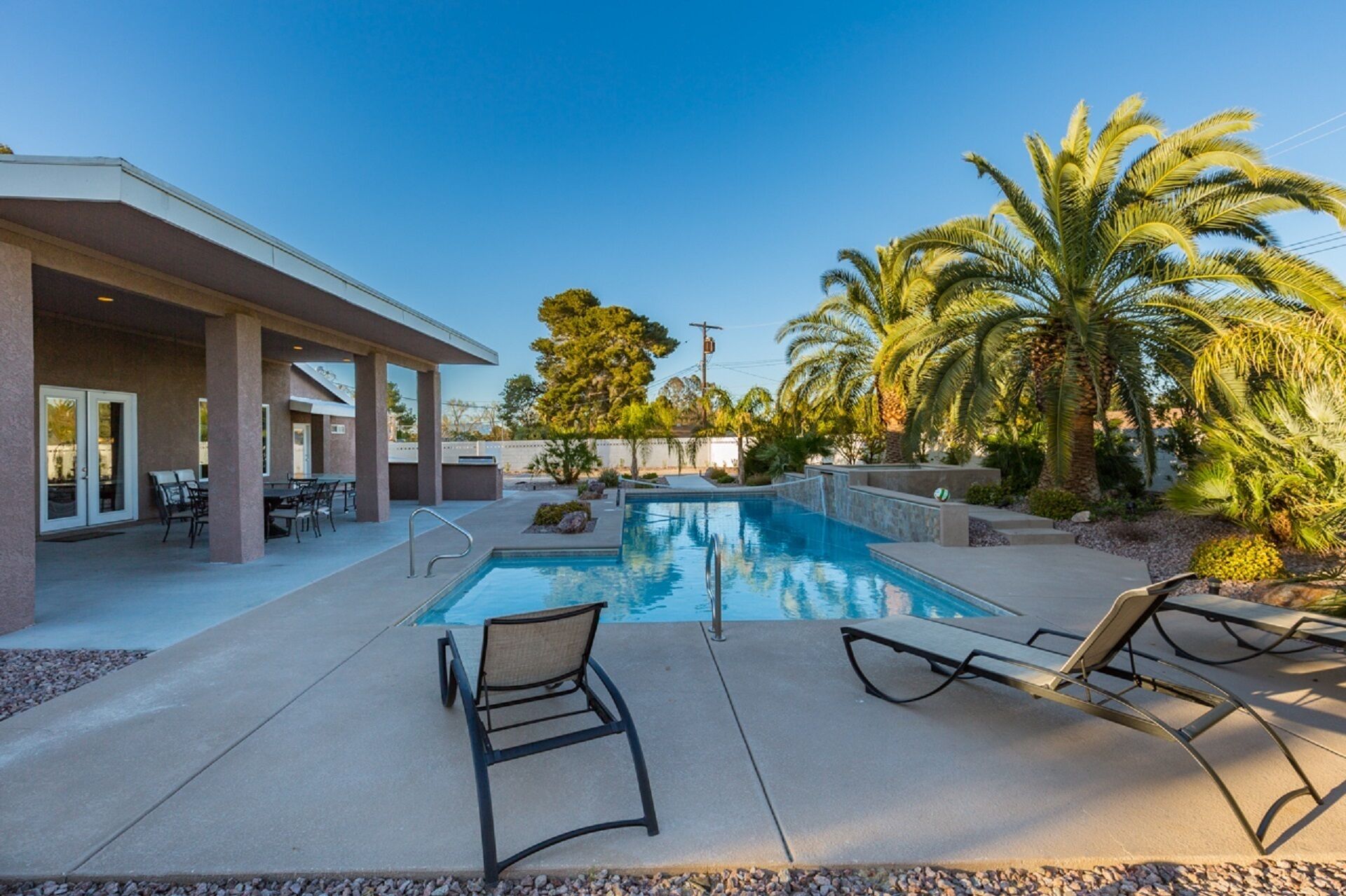 A pool area with lounge chairs, a covered patio, and palm trees.