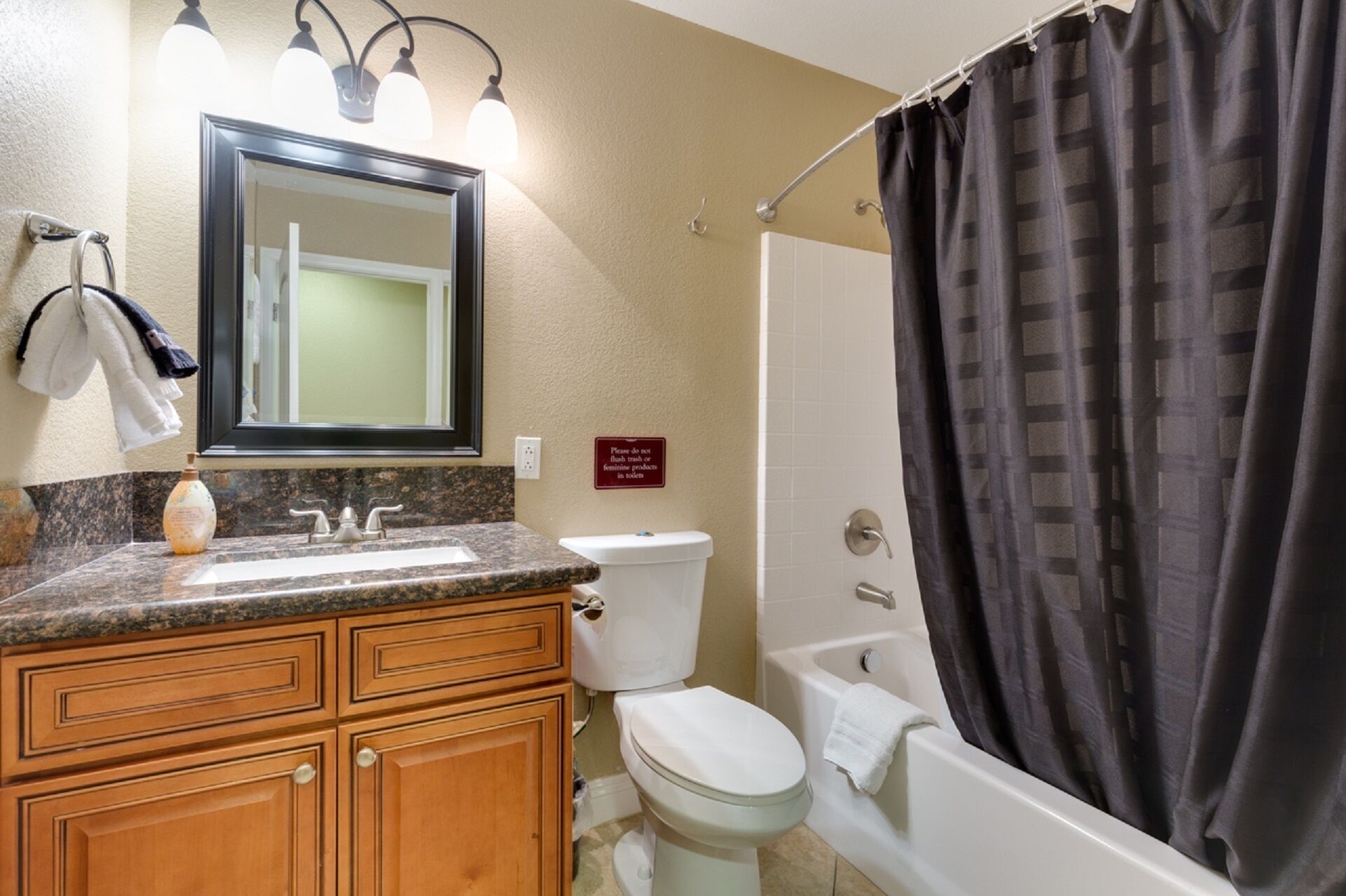 A bathroom with a granite countertop, wooden cabinets, a white toilet, a bathtub, and a shower curtain.