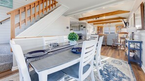 A spacious dining area with a wooden staircase, a kitchen in the background, and a view of the outdoors. - Oceanfront Home w/ Pool, Hot Tub, Game Room, Community Pool & Tennis/Pickleball (Avon)