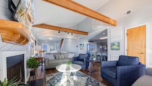 A spacious living room with a fireplace, a round coffee table, and a large blue sofa. - Oceanfront Home w/ Pool, Hot Tub, Game Room, Community Pool & Tennis/Pickleball (Avon)