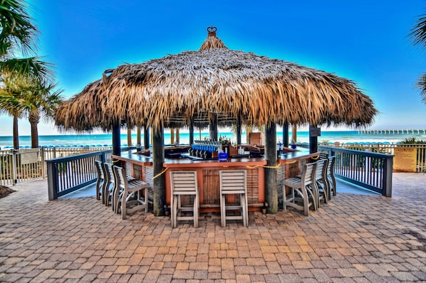 Relax by the ocean at our outdoor bar, featuring a thatched roof and bar stools.