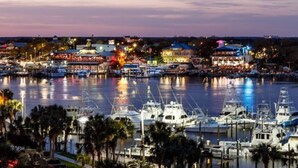Un port de plaisance où sont amarrés de nombreux bateaux, une tour imposante et une zone de restaurants au bord de l’eau.