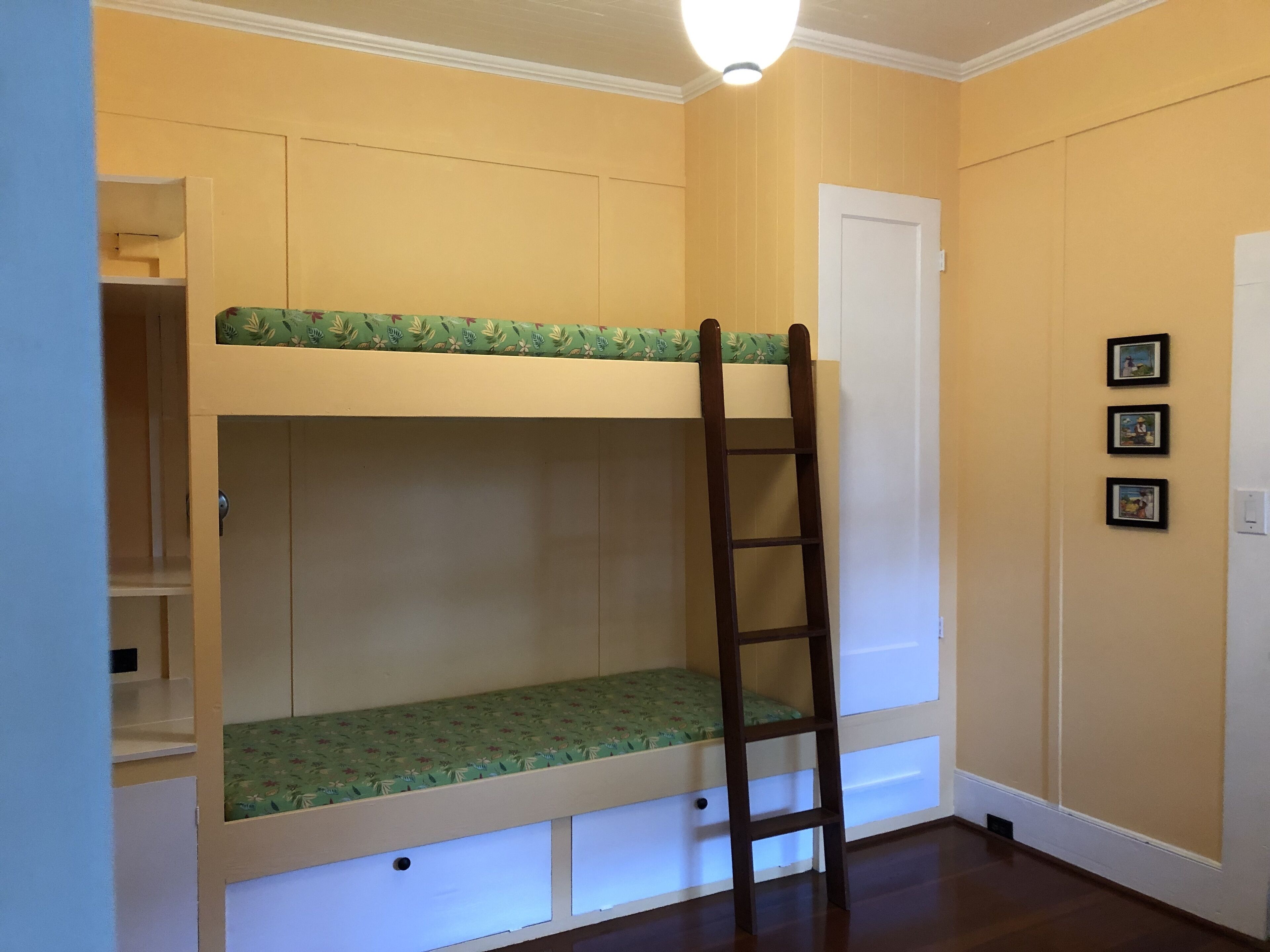 A bunk bed with a ladder, a white door, and three framed pictures on the wall.