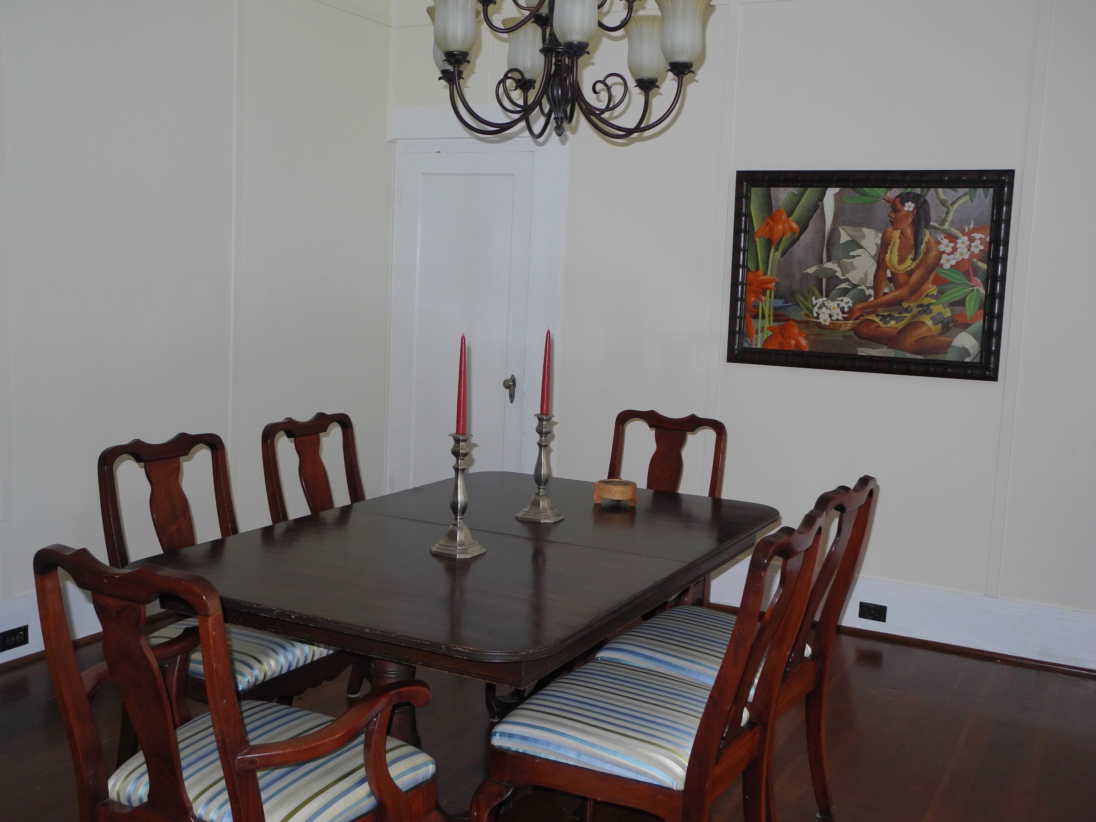 Un comedor con una mesa de madera oscura, seis sillas de madera con cojines a rayas, una araña y un cuadro enmarcado en la pared.