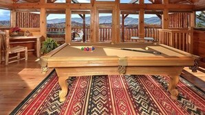 A pool table in a wooden room with large windows and a view of mountains.