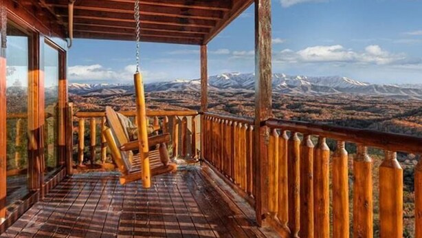 A wooden deck with a hanging chair overlooking a mountainous landscape.
