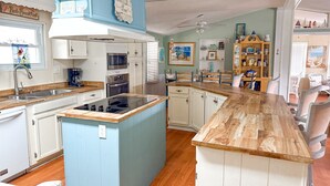 A kitchen with a central island, white cabinets, a blue accent wall, and a dining area with chairs. - Resort community, 6seater golf cart, dog friendly. Message for discount (Surfside)