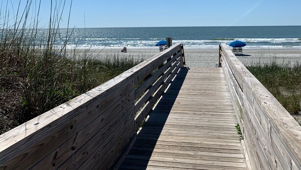 A wooden boardwalk leading to the beach with two blue umbrellas. - Resort community, 6seater golf cart, dog friendly. Message for discount (Surfside)