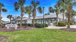 A modern building with a glass facade, palm trees, and a sign reading "OASIS POOL". - Resort community, 6seater golf cart, dog friendly. Message for discount (Surfside)